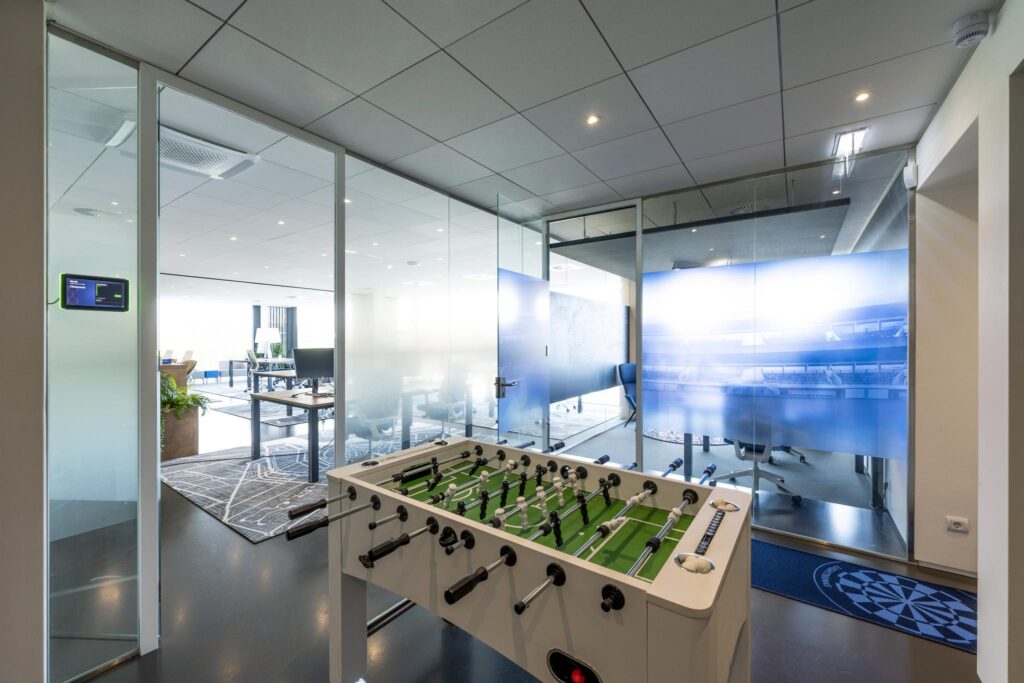 Modern office space with glass-walled meeting rooms and a foosball table in the foreground.